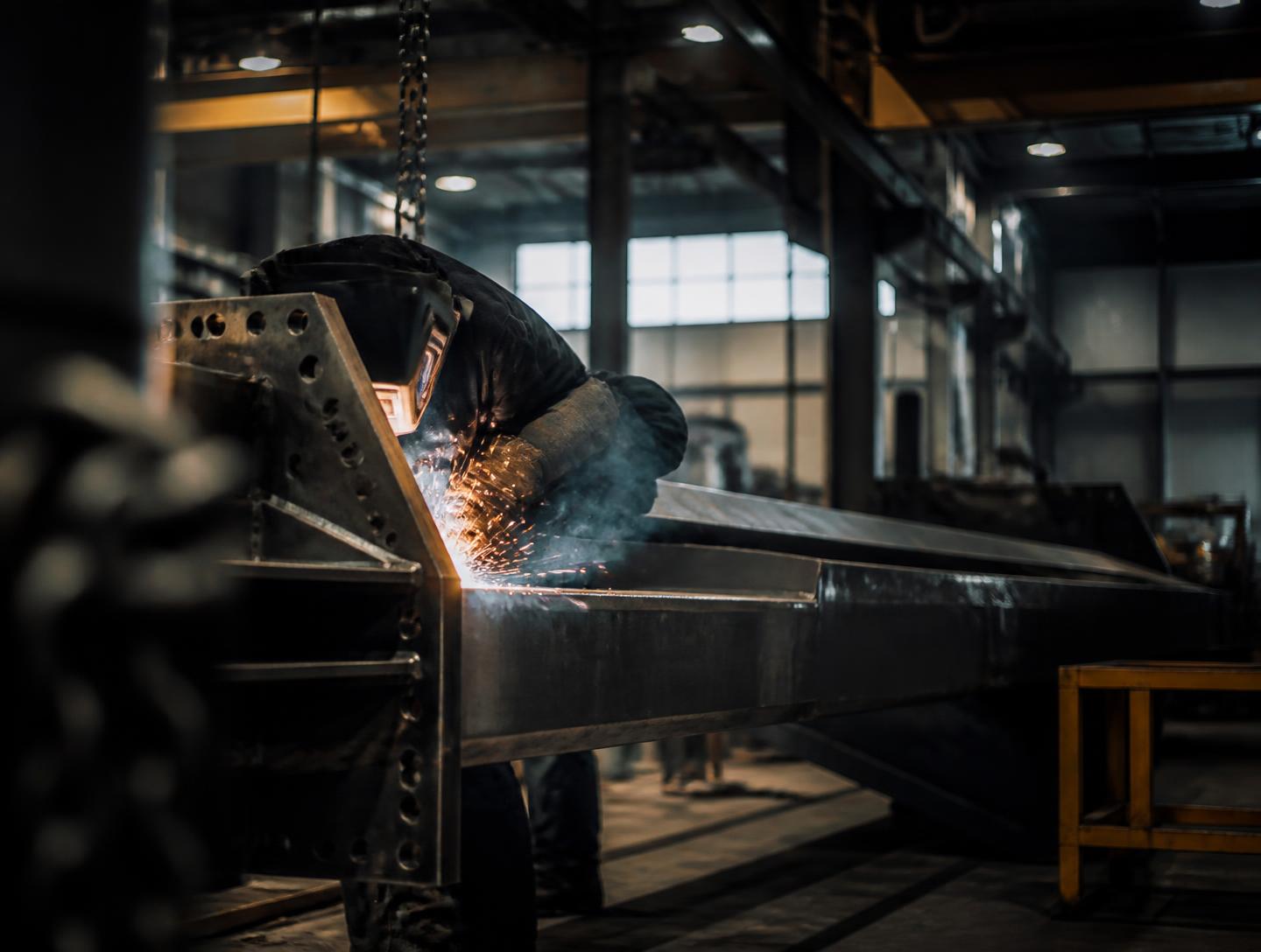 Welder joining a large steel assembly on the floor of a metal fabrication plant